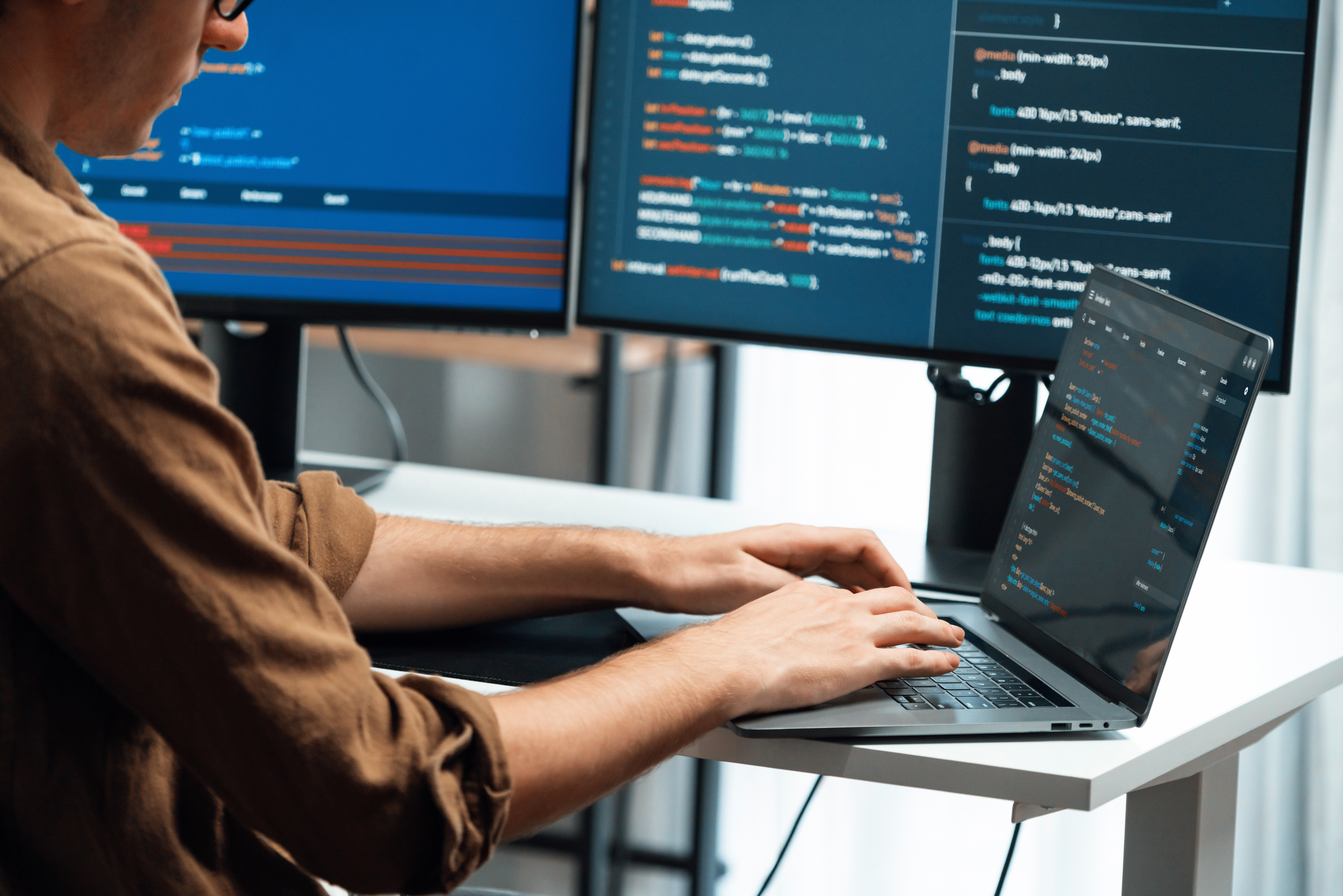 Man working on a laptop with monitors